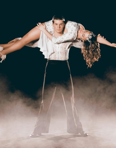 Elegant pair performing a dramatic dance lift surrounded by mystic smoke on stage.